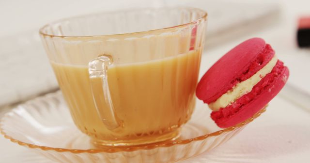 Featuring a delicate glass cup filled with tea paired with a vibrant pink macaron with creamy filling. Ideal for illustrating concepts related to tea time, cozy morning routines, gourmet snacks, and elegant dessert presentations. Suitable for use in hospitality, food blogs, cafes, and lifestyle promotional materials.