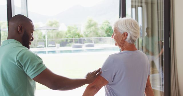 Image of happy african american male physiotherapist exercising with caucasian senior woman. seniors health and nursing home lifestyle concept.