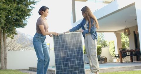 Women installing solar panel sunlit backyard poolside, teamwork for renewable energy