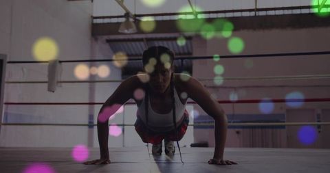 Female athlete doing push-ups in boxing ring with colorful bokeh, gritty industrial gym