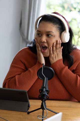 Surprised african american podcaster reacting live wearing headset and speaking into microphone