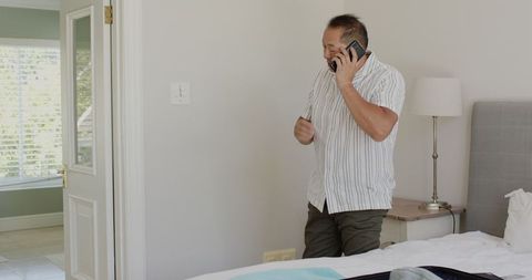Asian Man Organizing with Phone While Packing Suitcase at Home