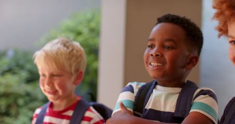 Happy diverse schoolchildren standing on porch with backpacks and striped shirts