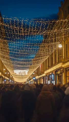Vertical Crowd Walking Illuminated Shopping Street Under Festive String Lights at Dusk