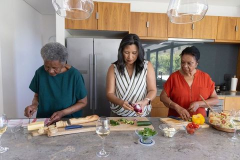 Multigenerational african american women chopping and assembling salad at kitchen island