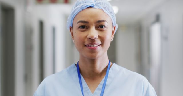 Image portrait of happy biracial female medical worker in surgical cap laughing in hospital corridor. Hospital, medical and healthcare services.