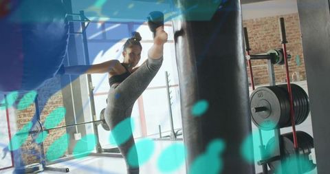 Female athlete delivering high kick to heavy bag in sunlit gym studio