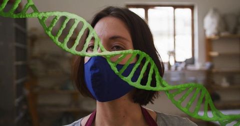 Female ceramic artist wearing blue mask and apron with green dna helix in pottery studio