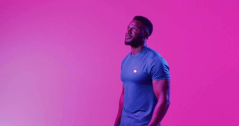 Standing muscular man wearing fitted blue athletic tee against magenta gradient backdrop