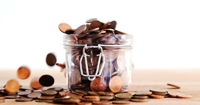 Coins are spilling out of an overflowing glass jar onto a surface, symbolizing abundance or financial savings. Capturing the essence of money management and savings growth, the image resonates with themes of personal finance and investment.