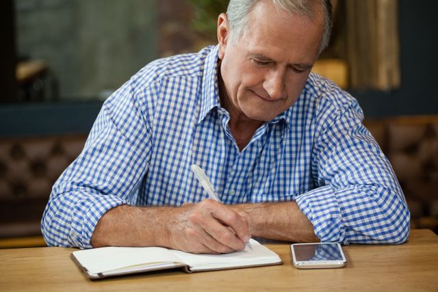 Senior man writing on diary at table while sitting in cafe