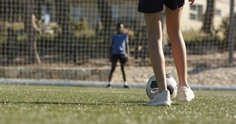 Teen girl taking penalty kick while boy goalkeeper defending on soccer field