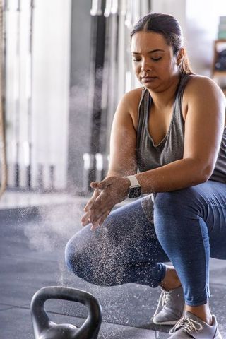 Kettlebell chalking and focus: woman preparing for strength training, wearing smartwatch