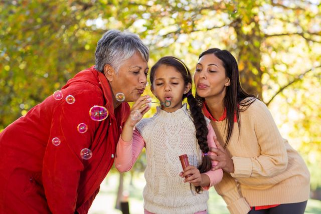 Daughter with mother and grandmother blowing bubbles at park