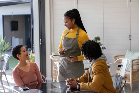 Friendly server taking order on tablet while chatting with smiling diners at cafe patio