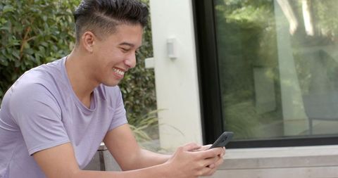 Young Asian Man Enjoying Smartphone by Modern Building Outdoors