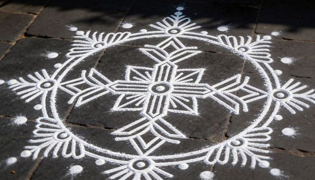 Displaying white rangoli mandala on dark stone tiles with chalk traces and leaf shadows