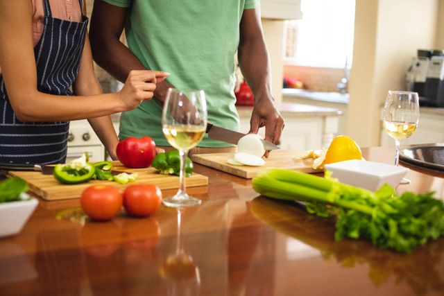 Midsection of biracial young woman assisting african american man cutting vegetables in kitchen. unaltered, couple, healthy food, drink, preparation, apron, lifestyle and domestic life concept.