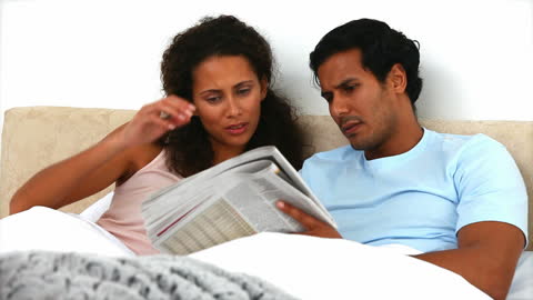 Couple Reading Newspaper Together in Comfortable Bed