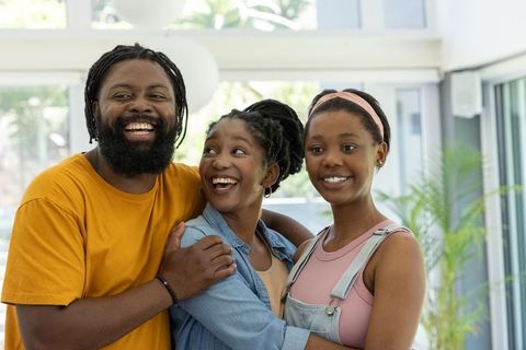 African american family hugging and laughing in sunlit living room with father and teen daughters