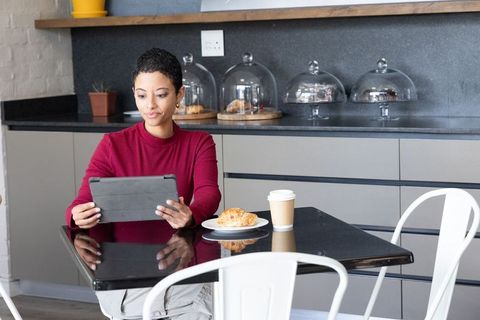 African american woman using tablet, enjoying coffee and croissant in cafe workspace