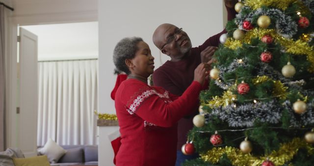 Senior African American couple decorating Christmas tree with ornaments and lights indoors. Perfect for holiday-themed content, promoting family activities, and celebrating Christmas traditions. Suitable for use in holiday greeting cards, seasonal advertising, and family-oriented promotions.