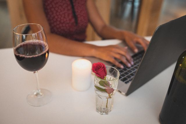 Midsection of biracial woman writing on laptop and having red wine. friends talking to each other online sitting in a restaurant.