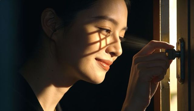 Smiling asian woman unlocking door with key in warm sunlight casting window grid shadow