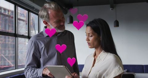 Middle-Aged Man and Woman Collaborating on Digital Device with Love Icons