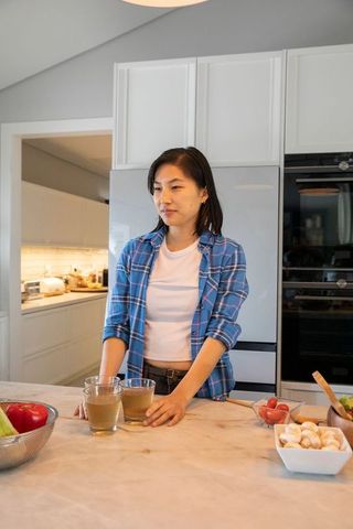 Asian Woman Holding Juice Glasses in Modern Kitchen