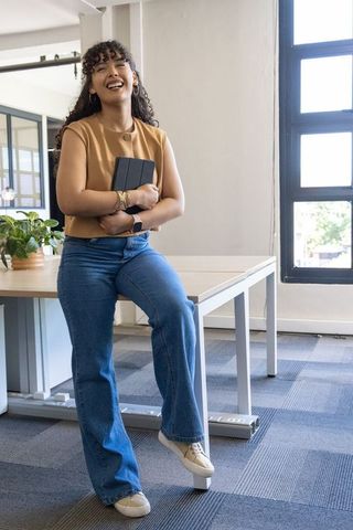 Laughing professional woman holding tablet in sunlit modern open workspace