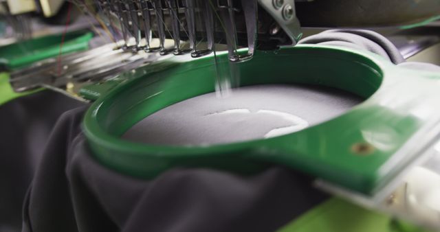 Close-up of an industrial embroidery machine in action, stitching a fabric with precise threads. This image can be used for illustrating topics related to textile manufacturing, garment production, and automated embroidery in various industrial contexts. It is ideal for articles, blogs, promotional materials, and educational content about sewing machinery and the textile industry.