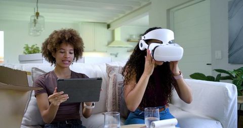 African friends testing VR headset while using tablet on sofa in modern bright living room