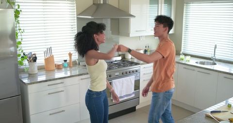 Young diverse couple fist-bumping and laughing in bright contemporary kitchen
