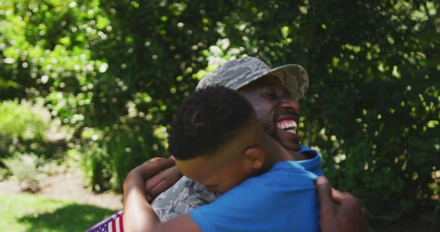 Happy african american soldier father hugging son with flag in garden. Military service, fatherhood, family and togetherness.