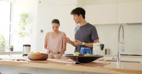 Young couple preparing smoothie and fruit bowls in sunlit modern minimalist kitchen