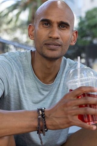 African american man enjoying iced drink on urban bench wearing beaded bracelet casual tee