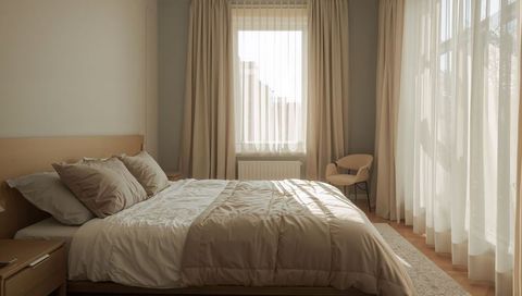 Sunlit minimalist bedroom with neutral bedding, sheer curtains and cozy wooden headboard