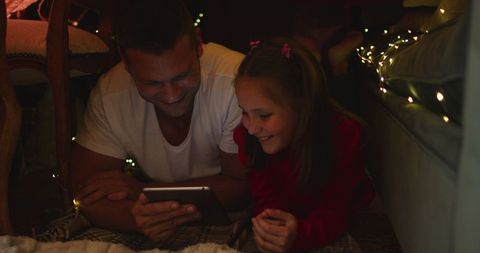 Father and Daughter Using Tablet in Blanket Fort with Festive Lights