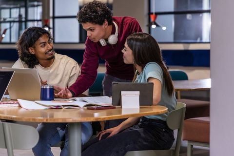 Diverse college students collaborating at round table with laptop and textbooks in study lounge