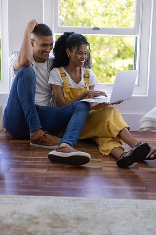 Young african american couple using laptop together by sunlit window on hardwood floor
