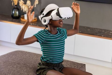 African girl wearing white vr headset reaching out in modern living room for virtual play