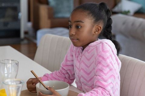 African american girl sitting at table eating breakfast from bowl in pink fleece cozy morning