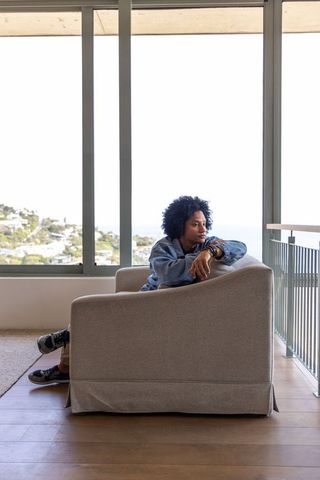 African american man sitting in armchair wearing denim jacket looking at ocean view