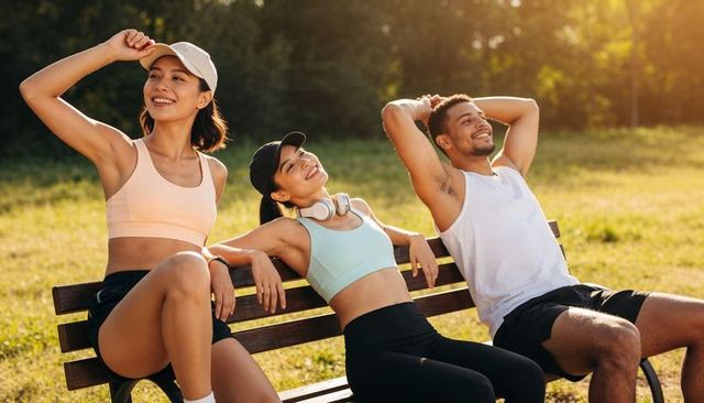 Friends relaxing on park bench after workout, smiling in activewear and caps