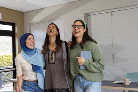 Diverse young women laughing and smiling studying together with tablet in bright classroom