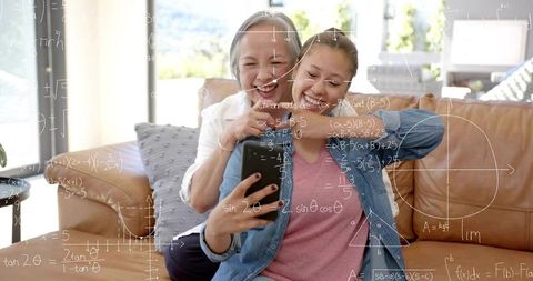 Mother and teen daughter learning together on couch with smartphone and math overlay