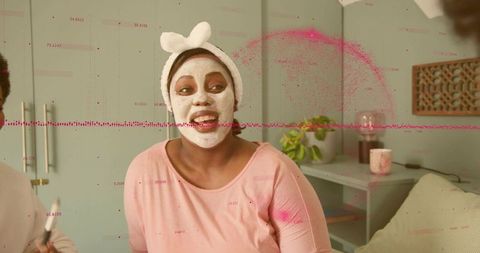 Smiling woman wearing white facial mask and headband enjoying cozy at-home skincare moment