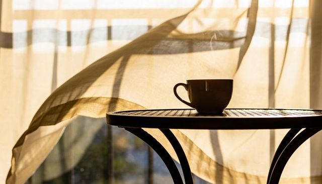 Morning sunlight streaming through sheer curtains with steaming cup on bistro table