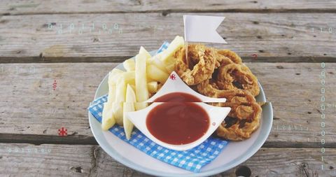 Crispy onion rings and fries with ketchup dip on rustic picnic table, digital overlay